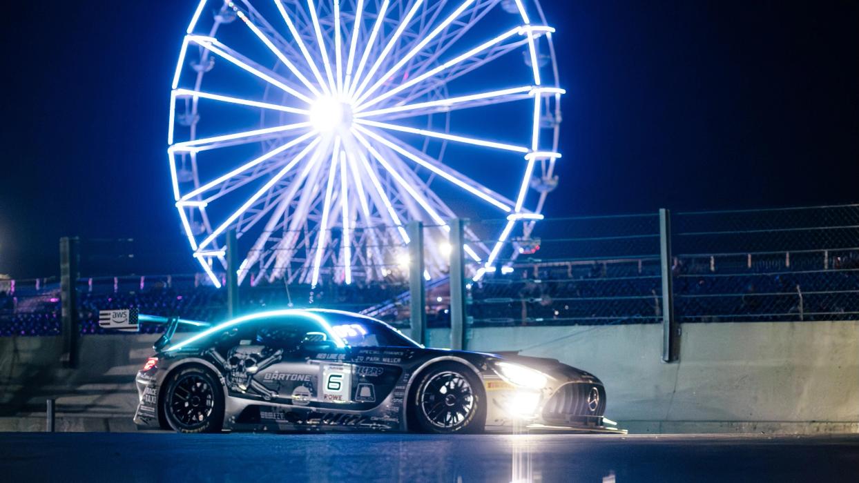 A Mercedes-AMG GT racing car is parked at night in front of an illuminated Ferris wheel